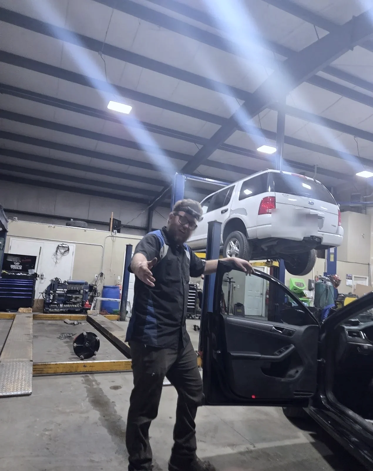 A technician in uniform at The Automotive Shop in Jerome, Idaho, with an SUV up on the lift